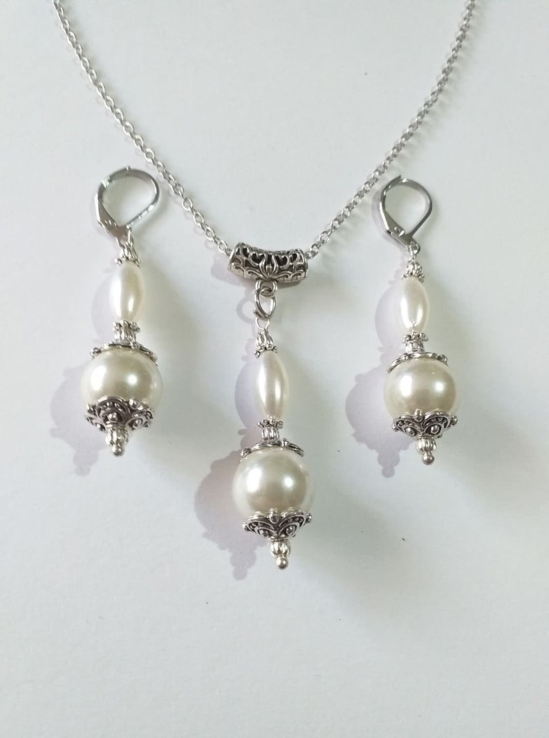 May include: A silver necklace and earrings set with white pearl beads and ornate silver accents.