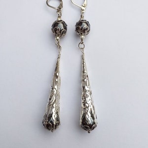 May include: A pair of silver dangle earrings with a black bead and a filigree design.