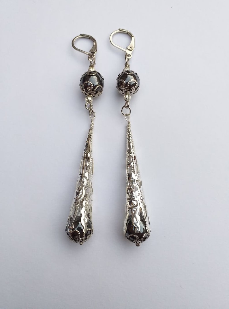 May include: A pair of silver dangle earrings with a black bead and a filigree design.