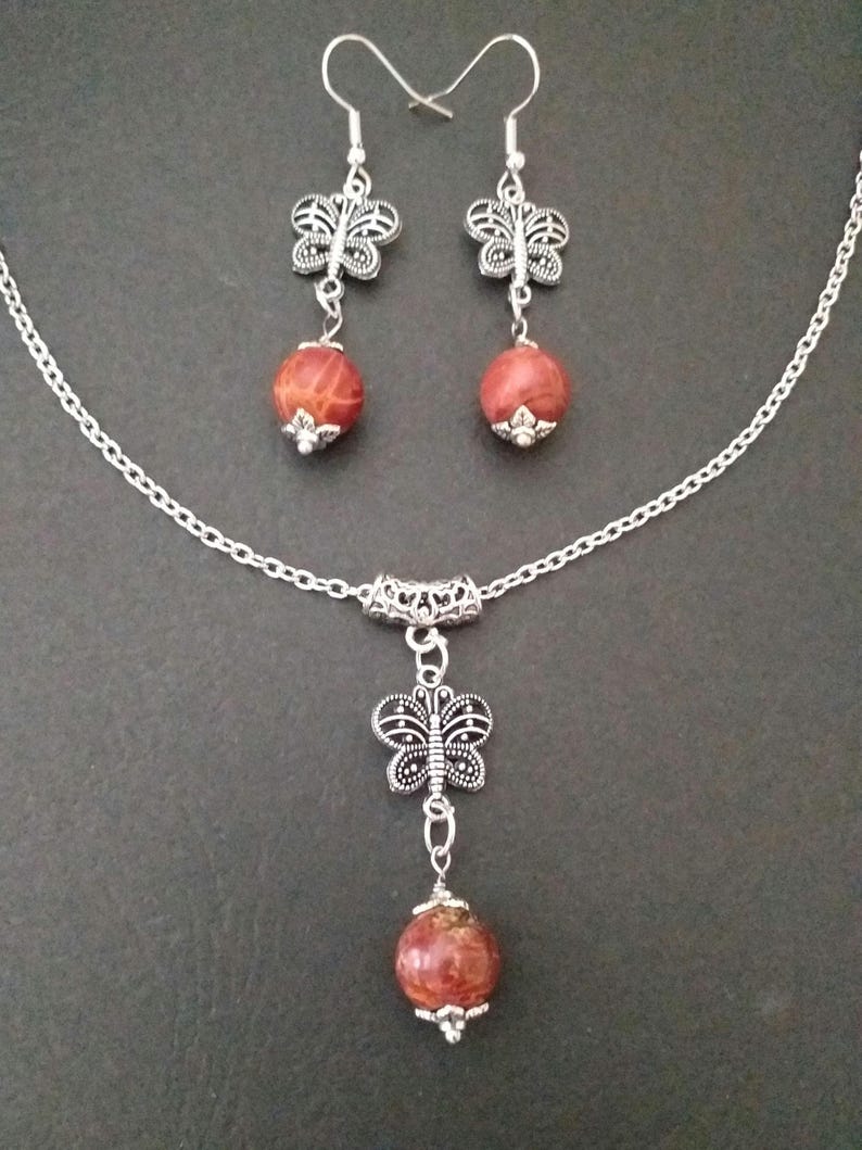 May include: A silver chain necklace with a red stone pendant and a silver butterfly charm. Matching earrings with red stones and butterfly charms.