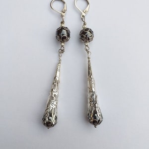 May include: A pair of silver dangle earrings with black beads and intricate filigree designs.