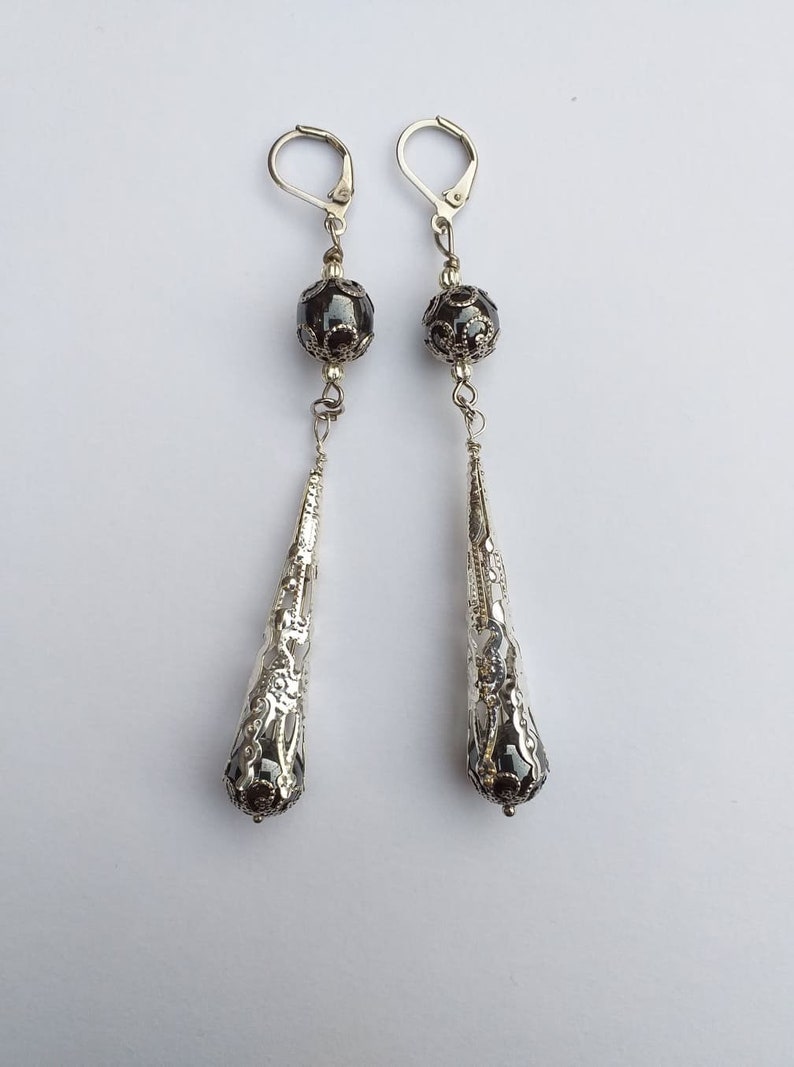May include: A pair of silver dangle earrings with black beads and intricate filigree designs.