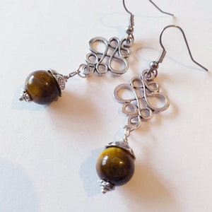 May include: Silver earrings with a delicate, intricate design and a round, brown tiger's eye gemstone dangle.