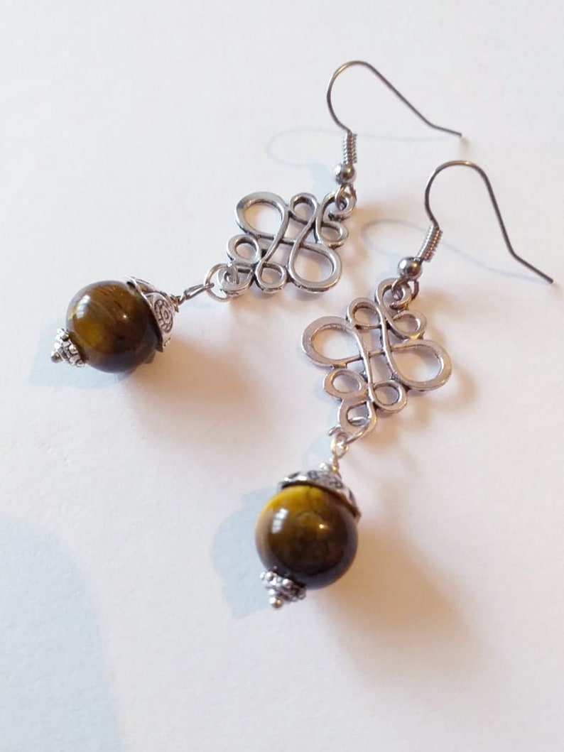 May include: Silver earrings with a delicate, intricate design and a round, brown tiger's eye gemstone dangle.