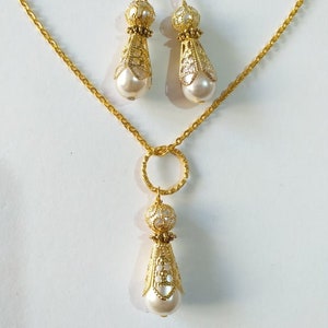 May include: A gold necklace with a delicate chain and a pendant featuring a pearl and ornate gold design. Matching earrings with pearl and gold accents.
