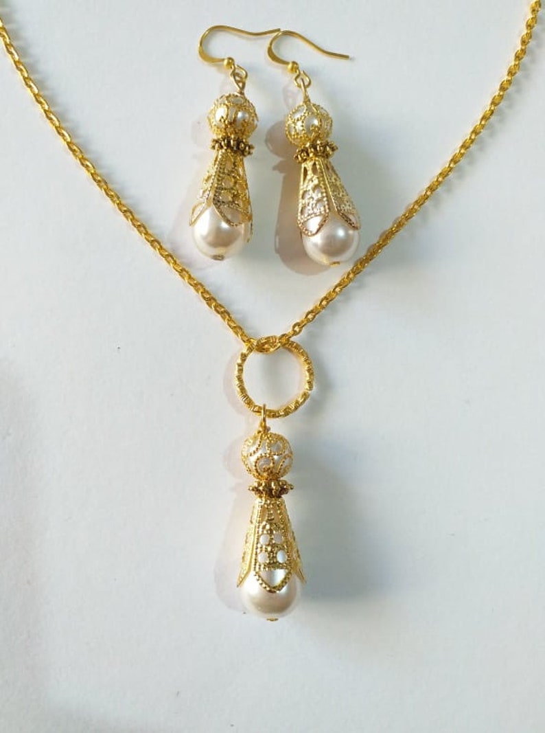 May include: A gold necklace with a delicate chain and a pendant featuring a pearl and ornate gold design. Matching earrings with pearl and gold accents.