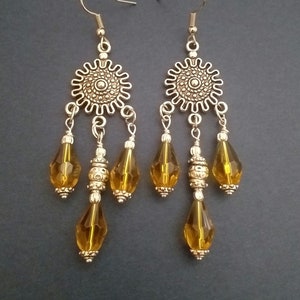 May include: A pair of silver dangle earrings with a round, ornate, silver centerpiece and three amber-colored teardrop-shaped crystals hanging from each earring.
