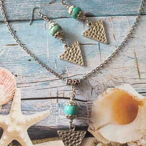 May include: A silver chain necklace with a turquoise bead and a silver triangle pendant. Matching earrings with turquoise beads and silver triangle pendants.