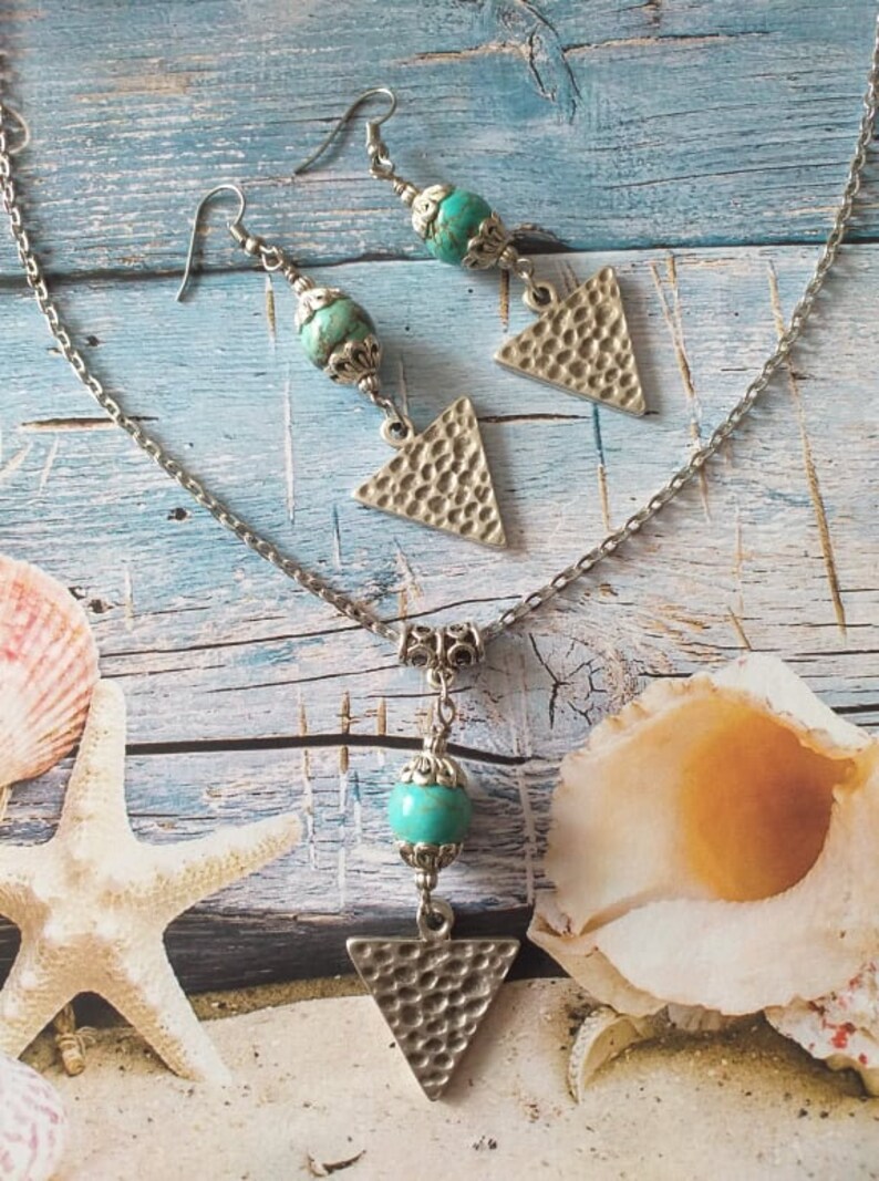 May include: A silver chain necklace with a turquoise bead and a silver triangle pendant. Matching earrings with turquoise beads and silver triangle pendants.