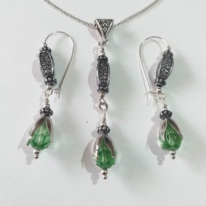 May include: A silver necklace and earrings set with green crystal teardrop pendants and ornate silver beads.