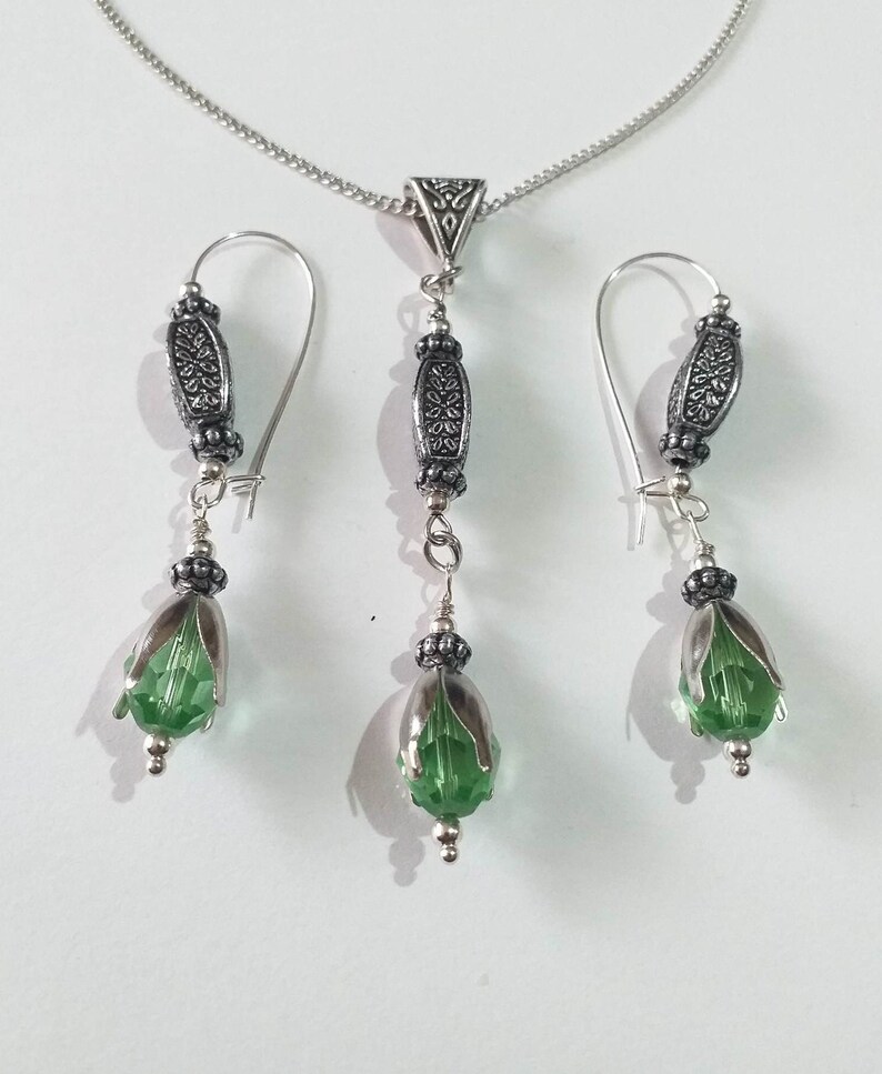 May include: A silver necklace and earrings set with green crystal teardrop pendants and ornate silver beads.