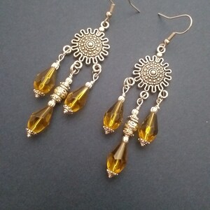 May include: A pair of silver dangle earrings with a round, ornate design at the top and three amber-colored teardrop-shaped beads hanging from each.