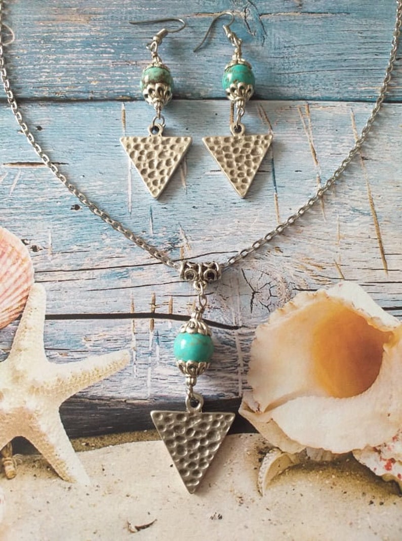May include: A silver necklace and earrings set with turquoise stones and triangle pendants. The necklace has a silver chain and a turquoise stone with a silver pendant in the shape of a triangle. The earrings have silver hooks and turquoise stones with silver triangle pendants.