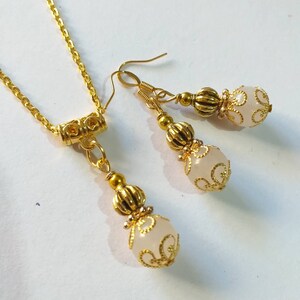 May include: A gold necklace and earrings set with white beads and intricate gold filigree designs.