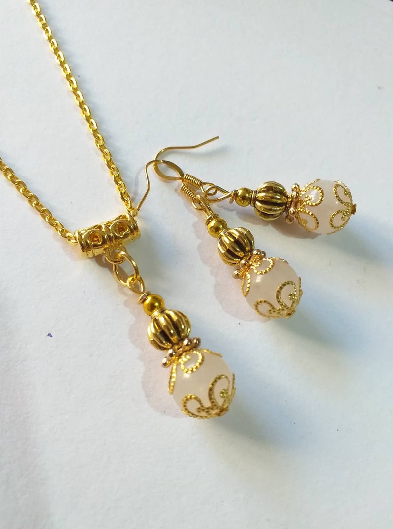 May include: A gold necklace and earrings set with white beads and intricate gold filigree designs.