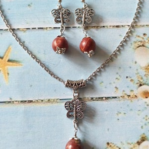 May include: A silver chain necklace with a red stone pendant and a silver butterfly charm. Matching earrings with red stones and silver butterfly charms.