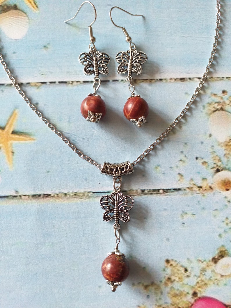 May include: A silver chain necklace with a red stone pendant and a silver butterfly charm. Matching earrings with red stones and silver butterfly charms.