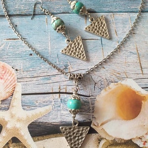 May include: A silver chain necklace with a turquoise bead and a textured triangle pendant. Matching earrings with turquoise beads and textured triangle pendants.