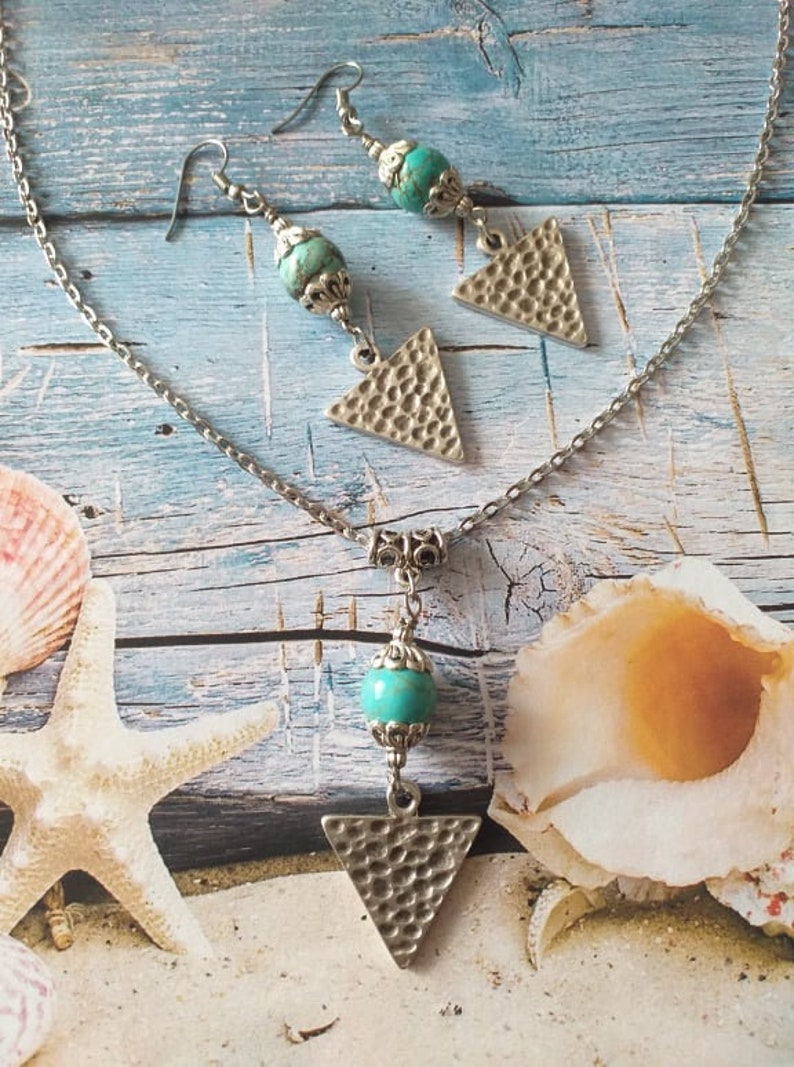 May include: A silver chain necklace with a turquoise bead and a textured triangle pendant. Matching earrings with turquoise beads and textured triangle pendants.
