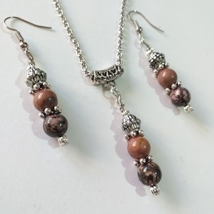 May include: A silver chain necklace with a silver pendant and three brown and black stone beads. Matching earrings with three brown and black stone beads.