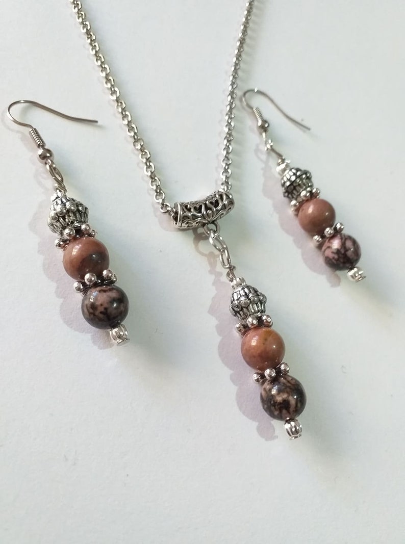 May include: A silver chain necklace with a silver pendant and three brown and black stone beads. Matching earrings with three brown and black stone beads.