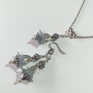 May include: A silver necklace and earrings set with grey flower-shaped charms and silver beads.