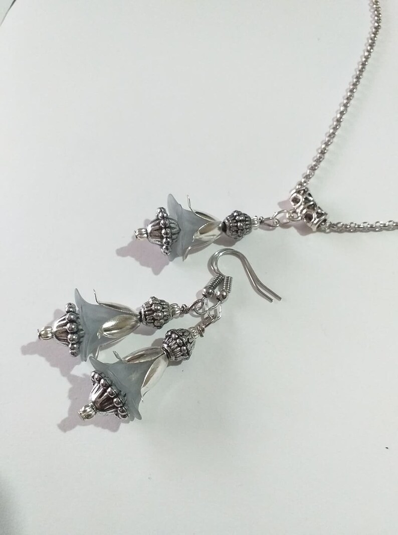 May include: A silver necklace and earrings set with grey flower-shaped charms and silver beads.
