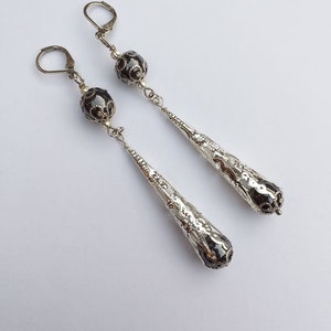 May include: A pair of silver dangle earrings with black beads and a textured teardrop design.