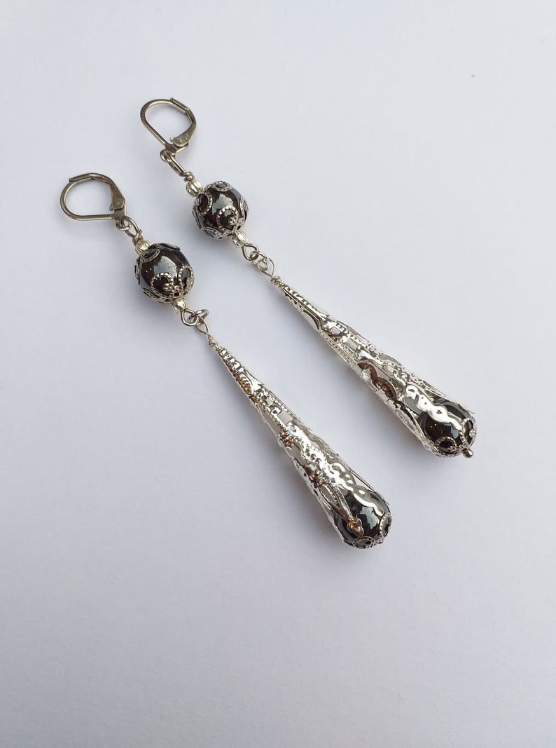 May include: A pair of silver dangle earrings with black beads and a textured teardrop design.
