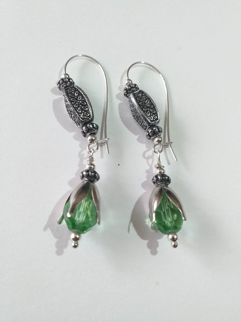 May include: Silver earrings with green crystal flower-shaped beads and silver filigree accents.