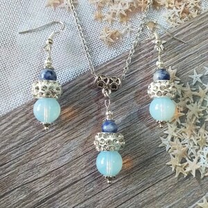 May include: A silver necklace and earrings set with blue and white beads. The necklace has a silver chain and a pendant with a blue and white bead. The earrings have a silver hook and a blue and white bead.