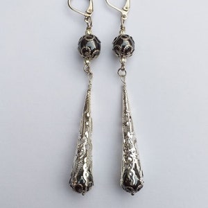 May include: A pair of silver dangle earrings with black beads and intricate filigree designs.