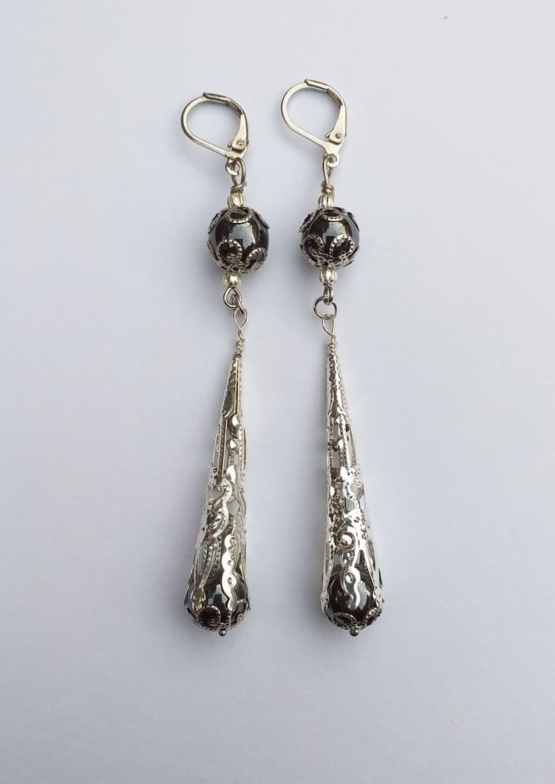 May include: A pair of silver dangle earrings with black beads and intricate filigree designs.