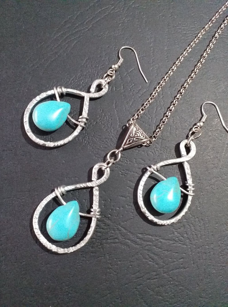 K&ouml;nnte beinhalten: Ein silbernes Halsketten- und Ohrring-Set mit T&uuml;rkis-Steinen. Die Halskette hat einen dreieckigen Anh&auml;nger mit einem komplizierten Design. Die Ohrringe sind tropfenf&ouml;rmig mit einem gedrehten Drahtdesign.