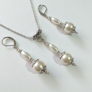 May include: A silver necklace and earrings set with white pearl beads and ornate silver accents.