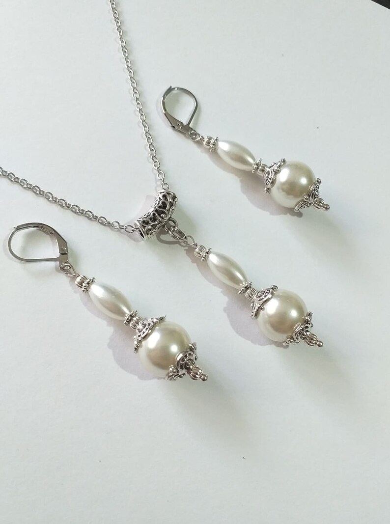 May include: A silver necklace and earrings set with white pearl beads and ornate silver accents.