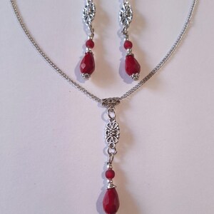 Puede incluir: Un collar de cadena de plata con un colgante de l&aacute;grima roja y un dije floral plateado. Aretes a juego con piedras de l&aacute;grima roja y dijes florales plateados.
