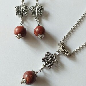 May include: A silver necklace and earrings set with red stone beads and butterfly charms.