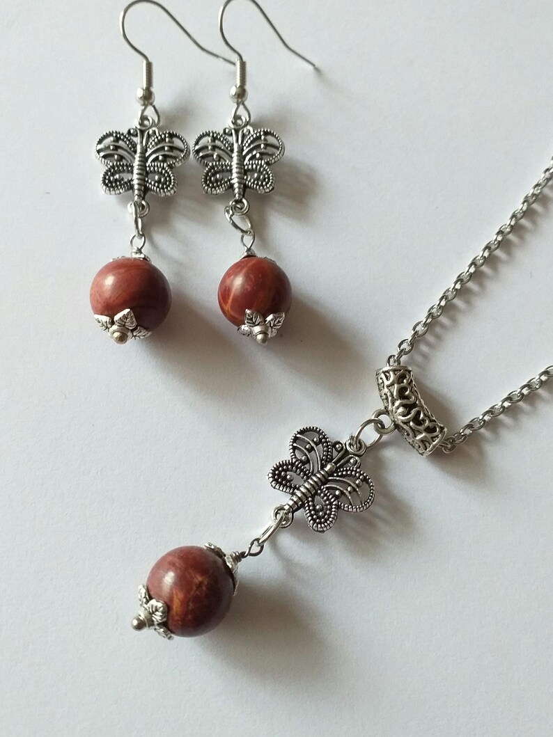May include: A silver necklace and earrings set with red stone beads and butterfly charms.