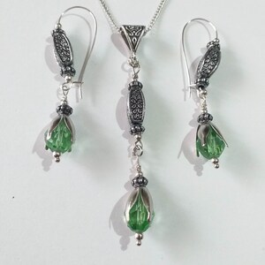 May include: A silver necklace and earrings set with green crystal teardrop pendants and ornate silver accents.