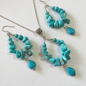 May include: A turquoise gemstone necklace and earrings set with silver accents. The necklace has a pendant with a silver ball and the earrings are drop earrings with a turquoise gemstone dangle.