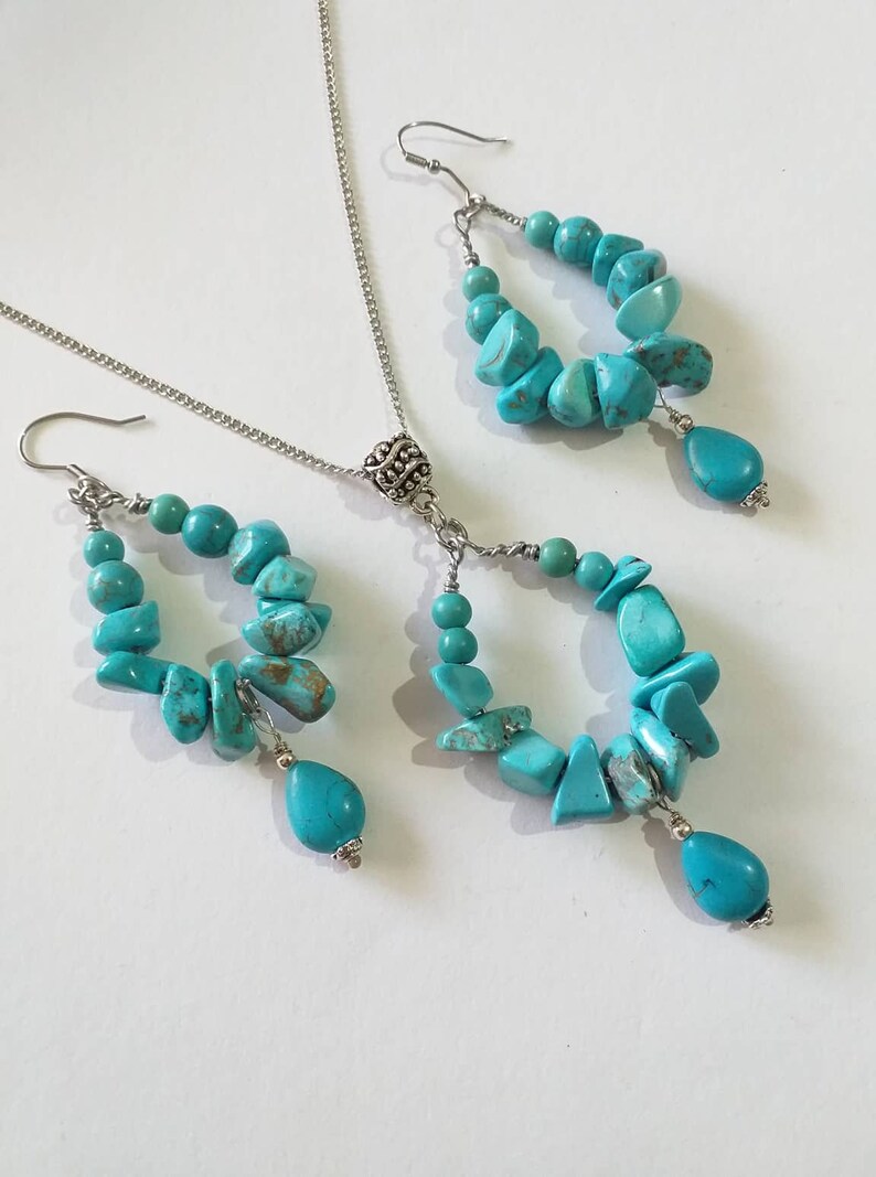 May include: A turquoise gemstone necklace and earrings set with silver accents. The necklace has a pendant with a silver ball and the earrings are drop earrings with a turquoise gemstone dangle.