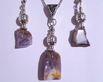 May include: A silver necklace and earrings set with amethyst stone pendants. The necklace has a silver chain and a silver pendant with a decorative design. The earrings have silver hooks and silver beads.