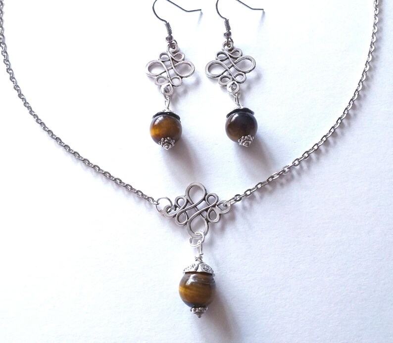 May include: A silver necklace and earrings set with a brown tiger's eye stone pendant and matching earrings. The necklace features a silver knot design and the earrings have a similar knot design.