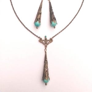 Puede incluir: Un conjunto de collar y pendientes de turquesa y bronce. El collar presenta una cadena delicada con un colgante en forma de l&aacute;grima con detalles intrincados. Los pendientes tambi&eacute;n tienen forma de l&aacute;grima con detalles a juego.