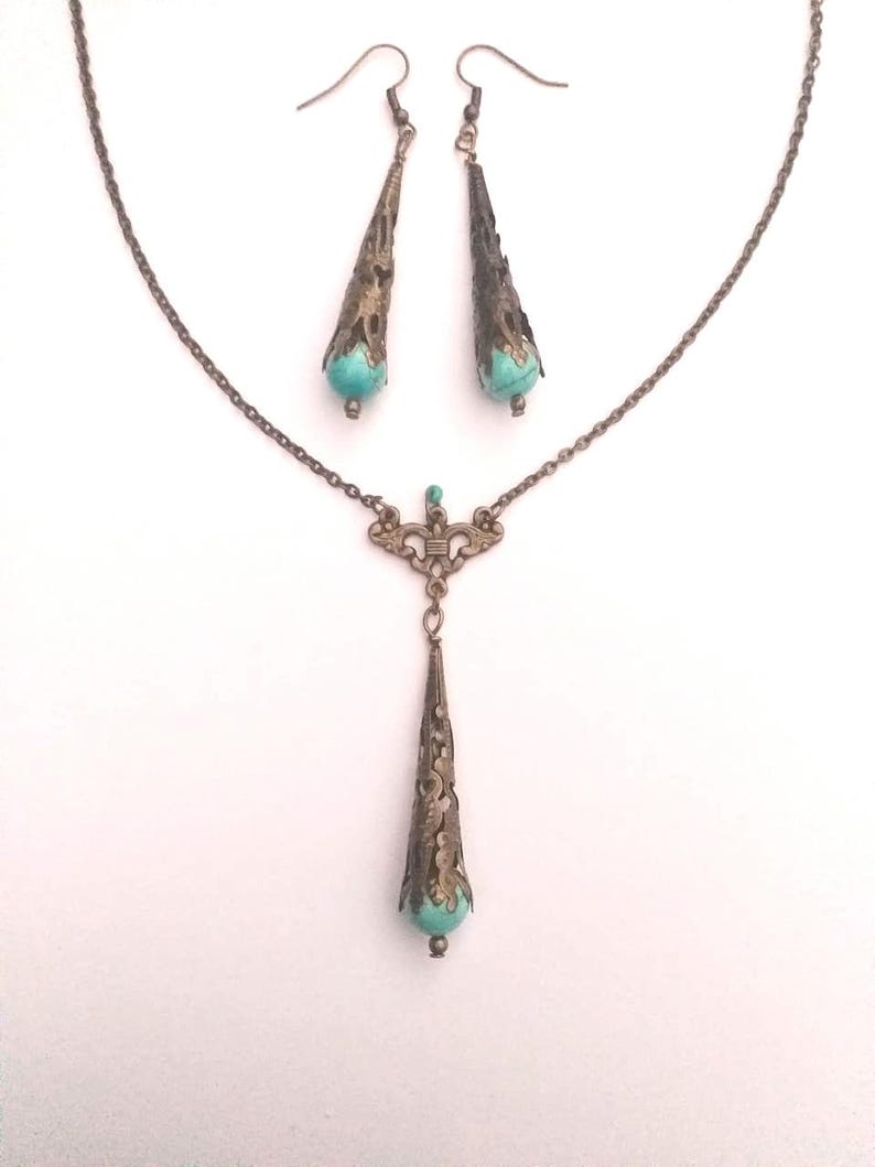 Puede incluir: Un conjunto de collar y pendientes de turquesa y bronce. El collar presenta una cadena delicada con un colgante en forma de l&aacute;grima con detalles intrincados. Los pendientes tambi&eacute;n tienen forma de l&aacute;grima con detalles a juego.