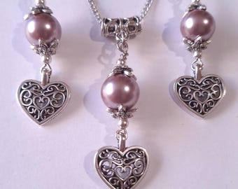 May include: A silver necklace and earrings set with a delicate heart pendant and a single pearl drop. The pearl is a soft mauve color.