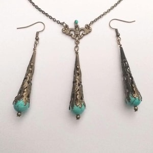 Puede incluir: Un conjunto de collar y pendientes de turquesa y bronce. El collar tiene un delicado dise&ntilde;o de filigrana y un colgante en forma de l&aacute;grima con una piedra turquesa. Los pendientes tambi&eacute;n son de forma de l&aacute;grima con piedras turquesa.