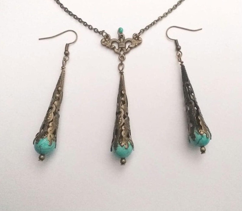 Puede incluir: Un conjunto de collar y pendientes de turquesa y bronce. El collar tiene un delicado dise&ntilde;o de filigrana y un colgante en forma de l&aacute;grima con una piedra turquesa. Los pendientes tambi&eacute;n son de forma de l&aacute;grima con piedras turquesa.