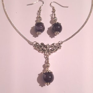 May include: A silver necklace and earrings set with a dark purple stone pendant and matching earrings. The necklace features a delicate silver chain and a decorative pendant with a floral design.